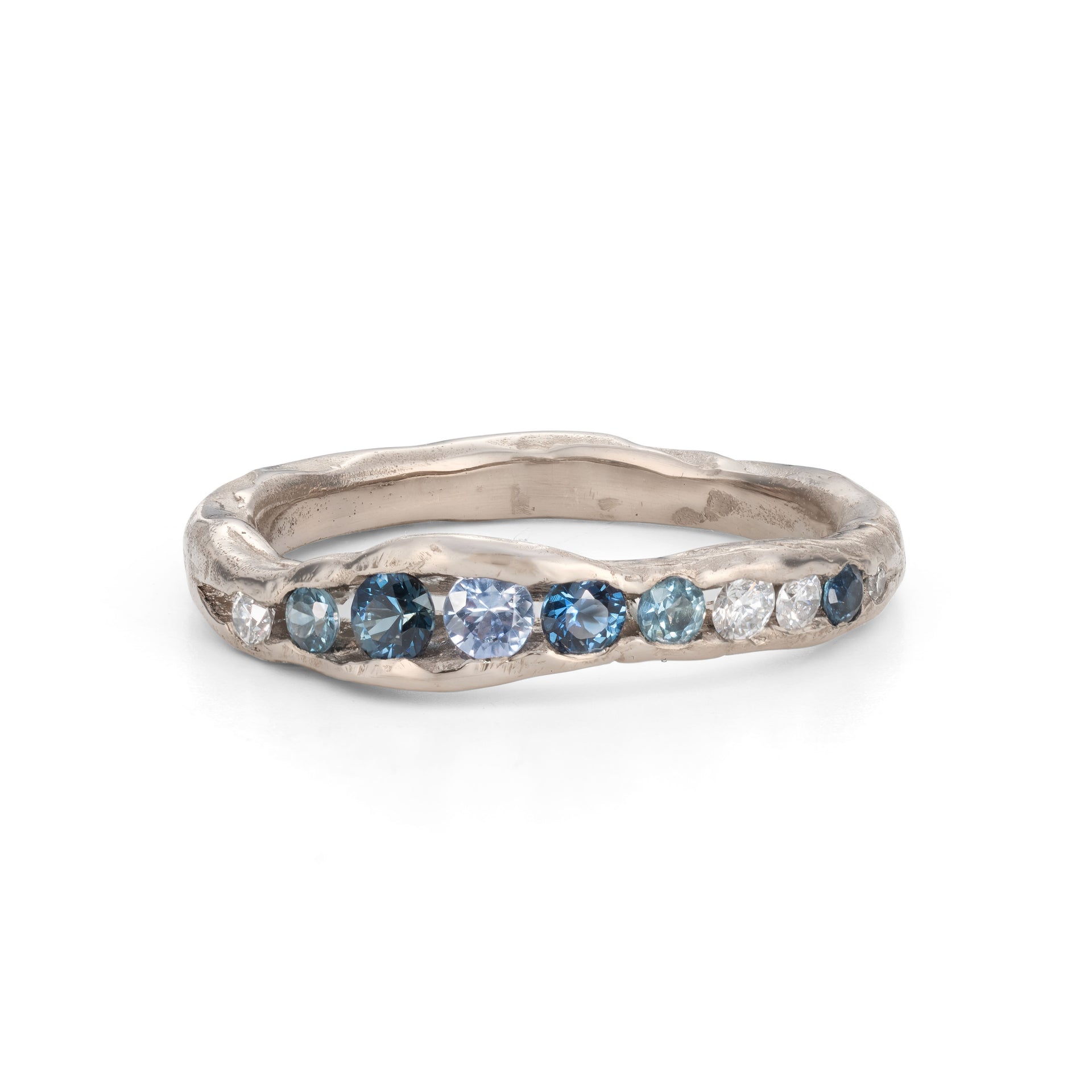 A channel forms a valley in this solid band of 18ct white gold, natural teal sapphires nestling in the sea worn crease. By Emily Nixon.