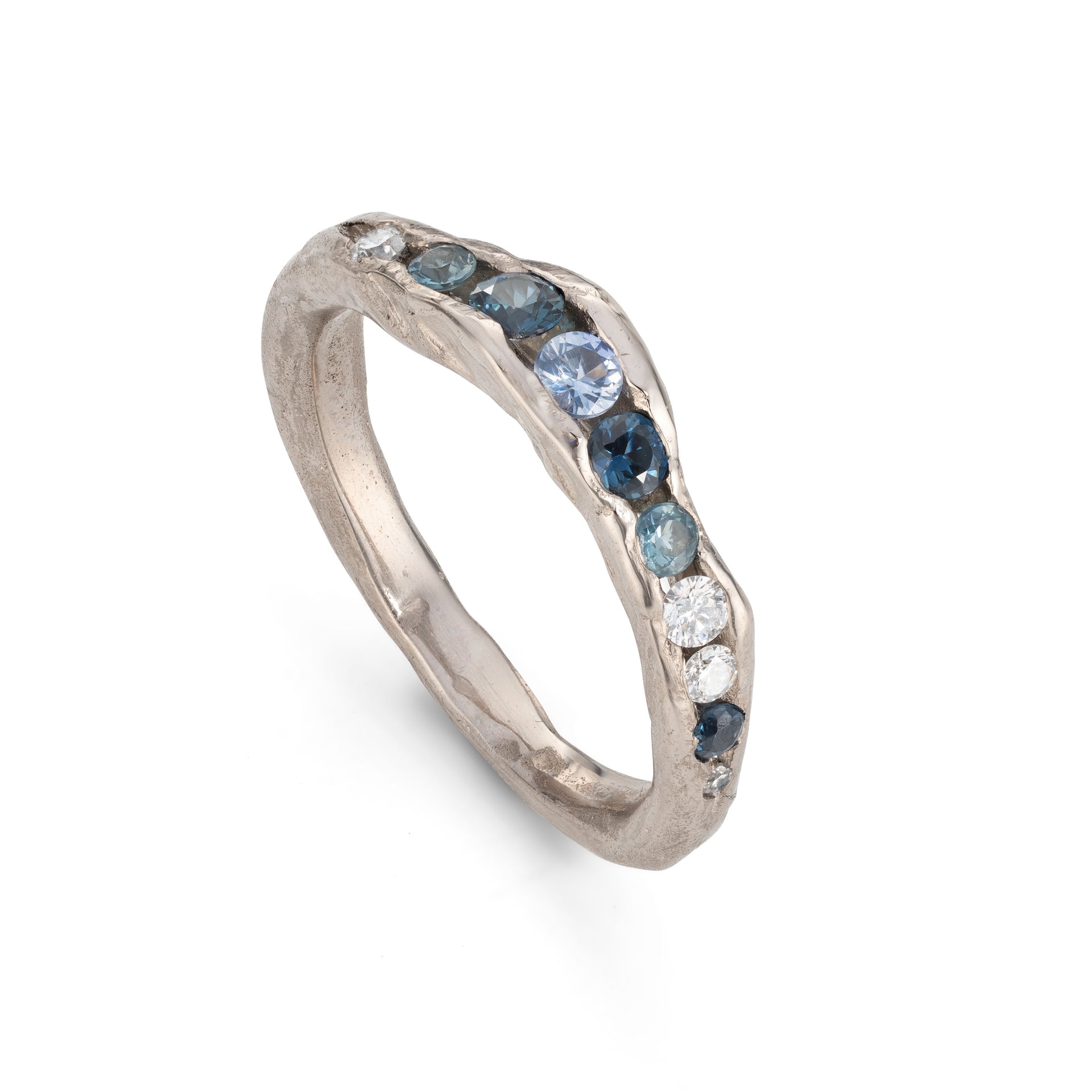 A channel forms a valley in this solid band of 18ct white gold, natural teal sapphires nestling in the sea worn crease. By Emily Nixon.