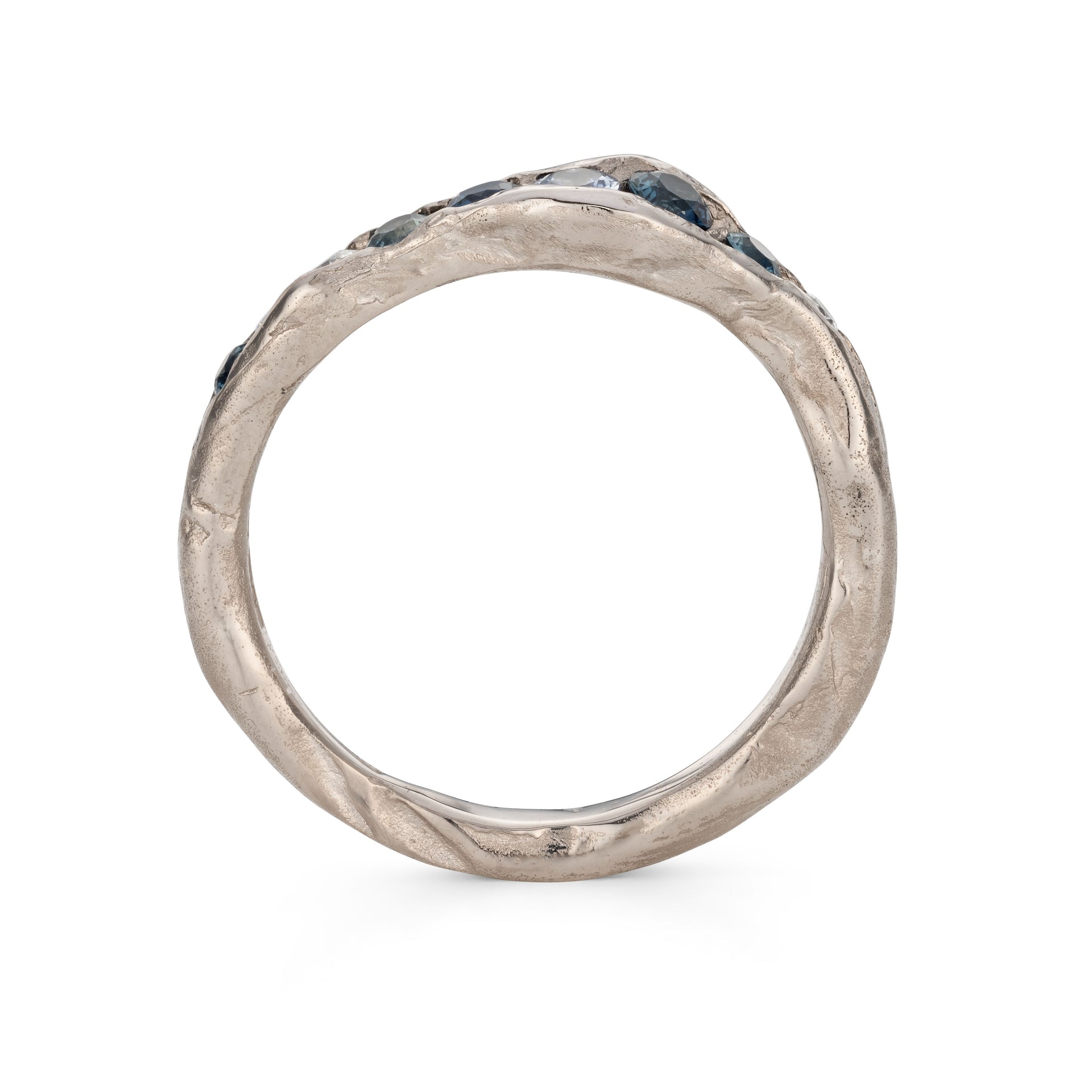 A channel forms a valley in this solid band of 18ct white gold, natural teal sapphires nestling in the sea worn crease. By Emily Nixon.