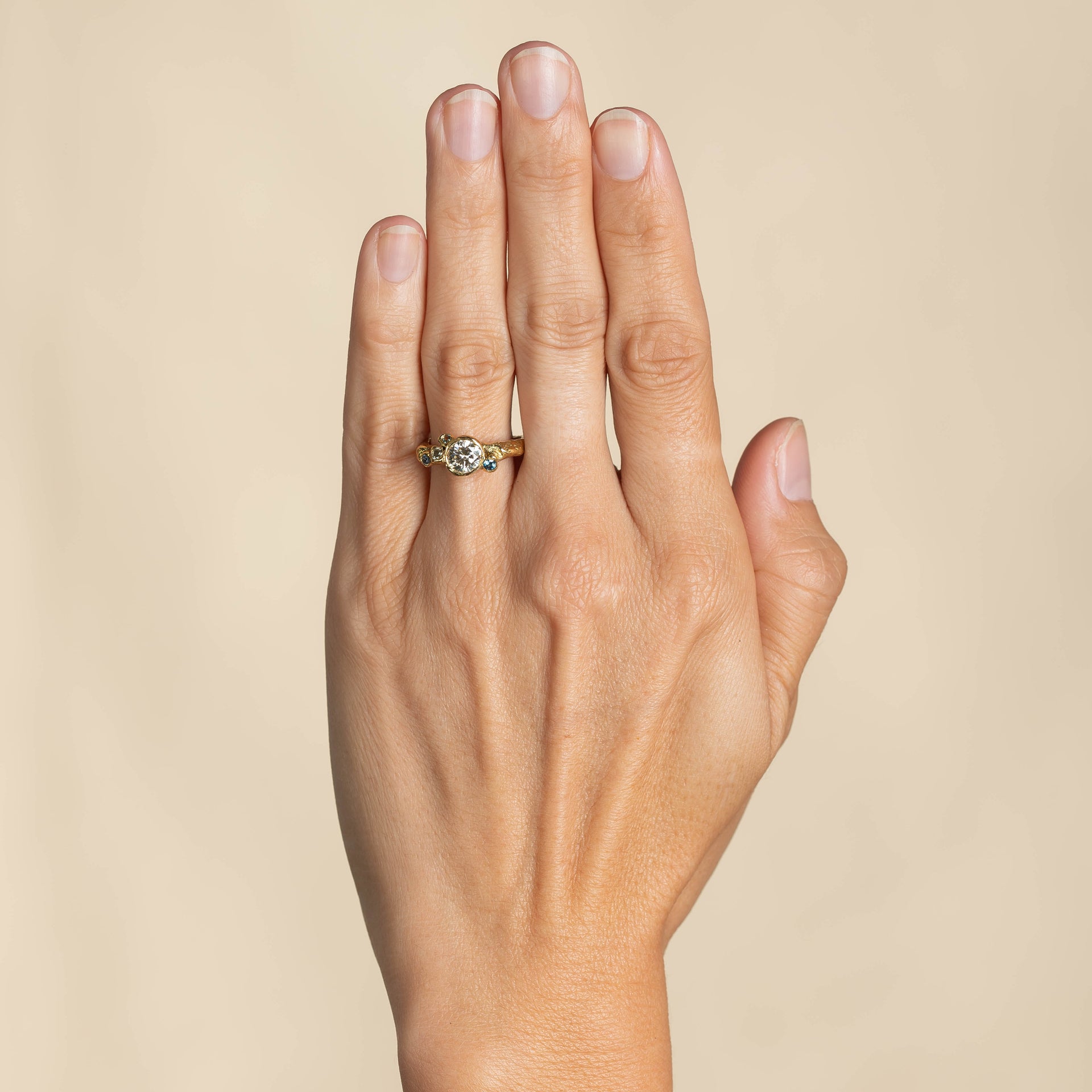 Rock pool sapphires perch around a pool of diamond white in perfect harmony. An artful engagement design with a hint of tradition in its focus on the central stone. Set in 18ct yellow gold By Emily Nixon.