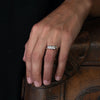 Diamond and platinum Emily Nixon engagement ring, shown on model with a platinum rock ring sitting next to it.