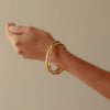 Model wearing a stack of uniquely sea worn Emily Nixon Craggy Bangles in 18ct gold 