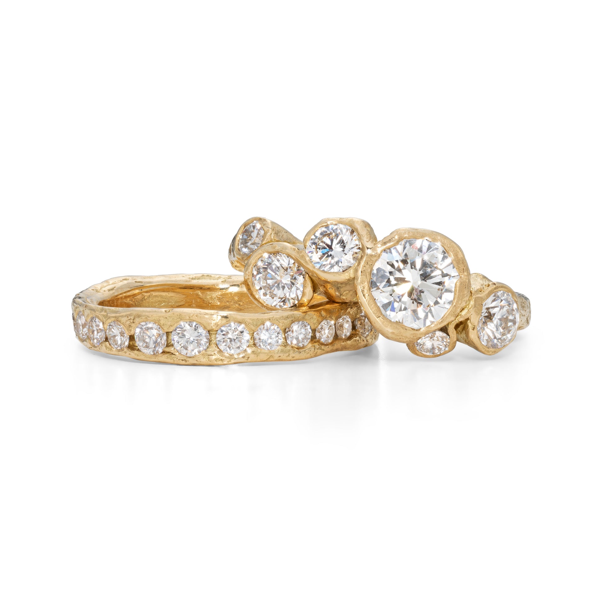 An 18ct gold and diamond engagement ring, with a large central diamond in the middle. Photographed next to a diamond channel ring, in a stack. Handmade by Emily Nixon.