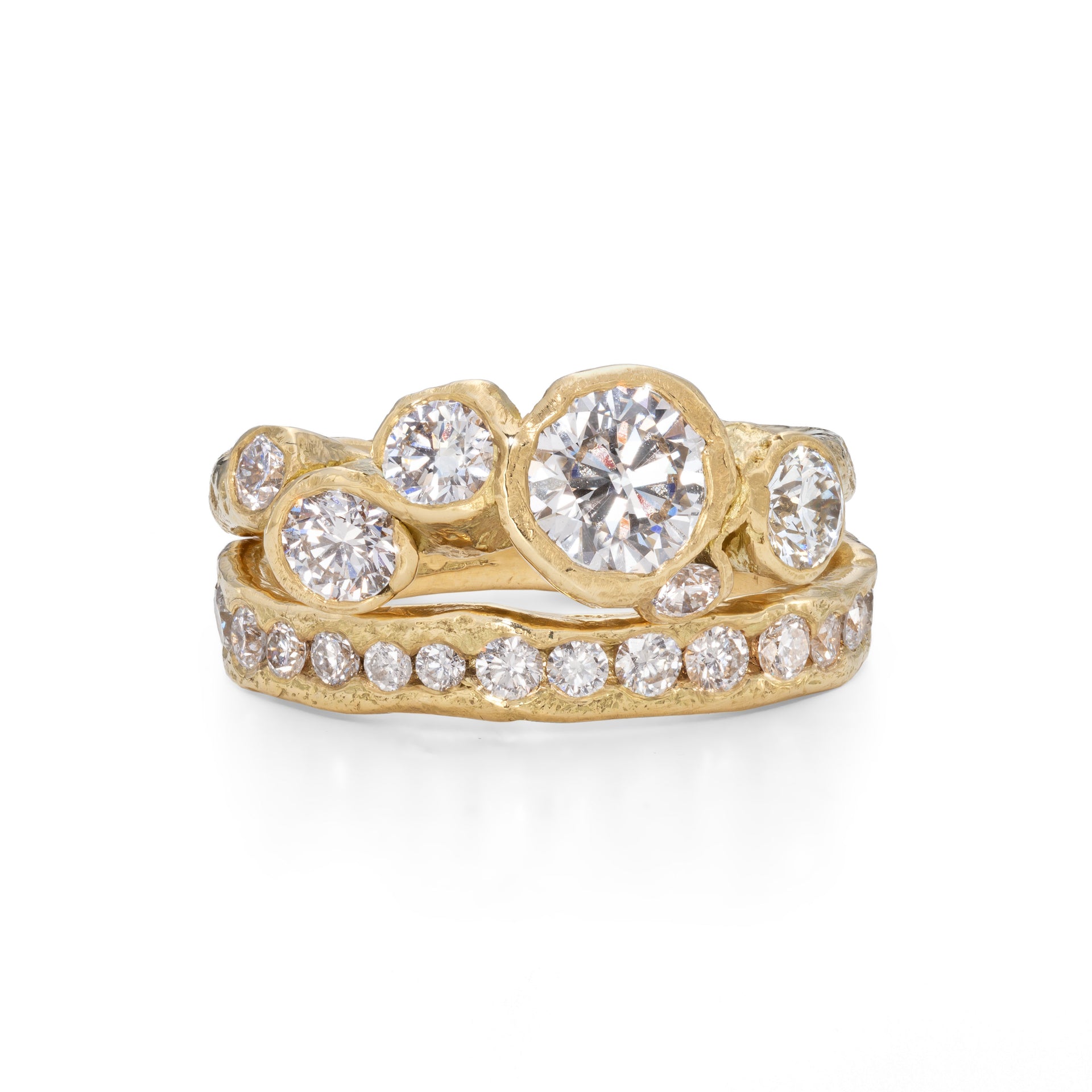 A diamond and gold engagement ring, set with 6 diamonds, with a central diamond in the middle. Photographed next to a gold channel ring, with diamonds set all the way around the band.