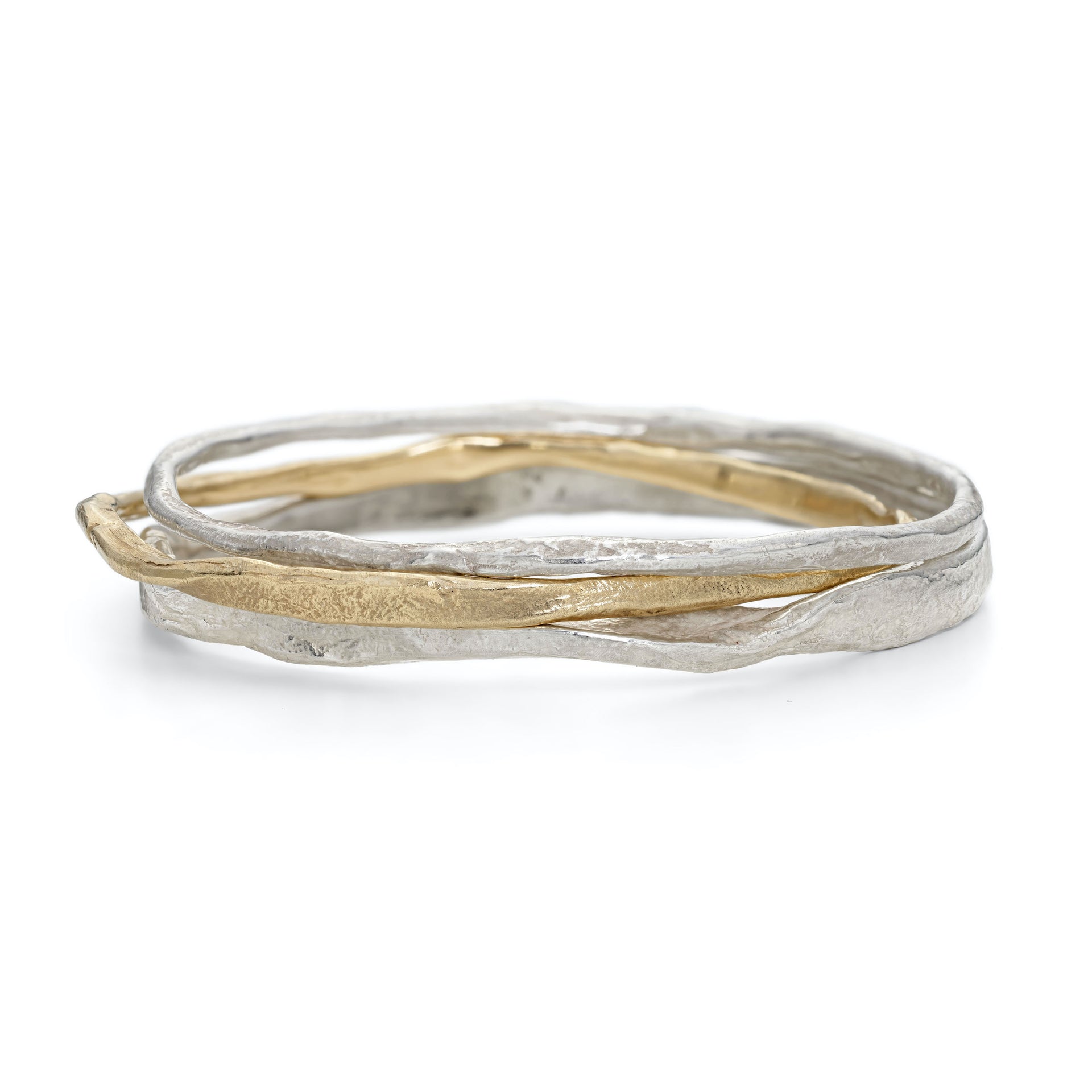 Stacking bangles in solid silver and gold. Chunky, irregular bangles in uneven widths have an organic texture and coastal character. Crafted in Cornwall by Emily Nixon.