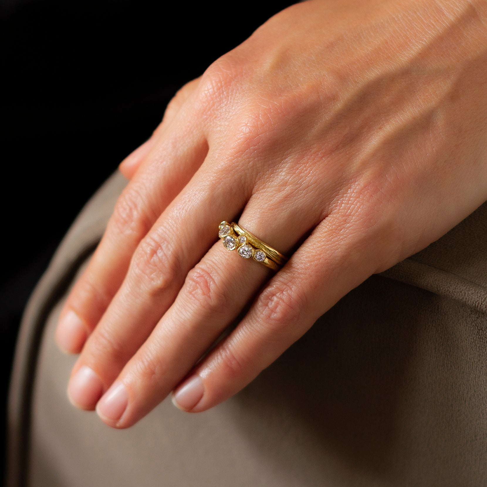 An unusual, alternative engagement ring by Emily Nixon. This ring has been set with 6 diamonds, in an organic design. Photographed on a models hand, sitting next to a gold ripple band.