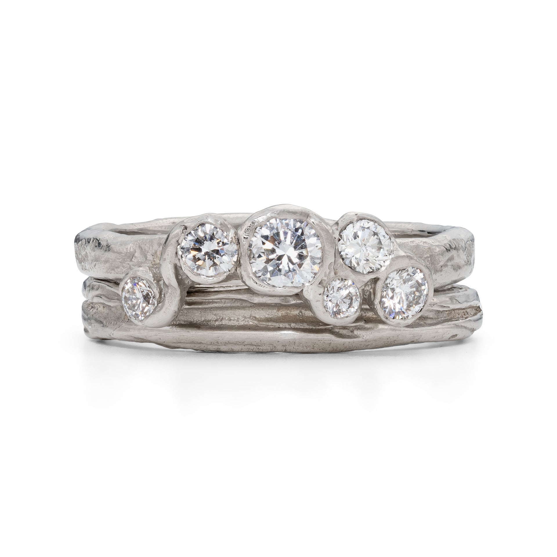 An alternative platinum engagement ring with 6 diamonds, sat next to a platinum ripple textured ring, by Emily Nixon.